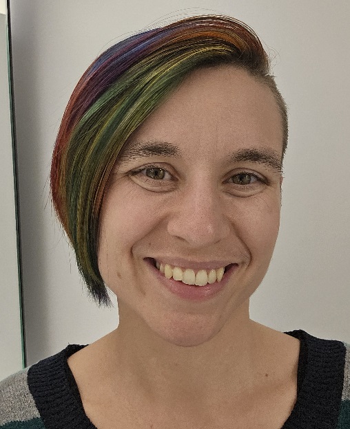 Marlena, a caucasian queer person with chin-length rainbow hair, smiling